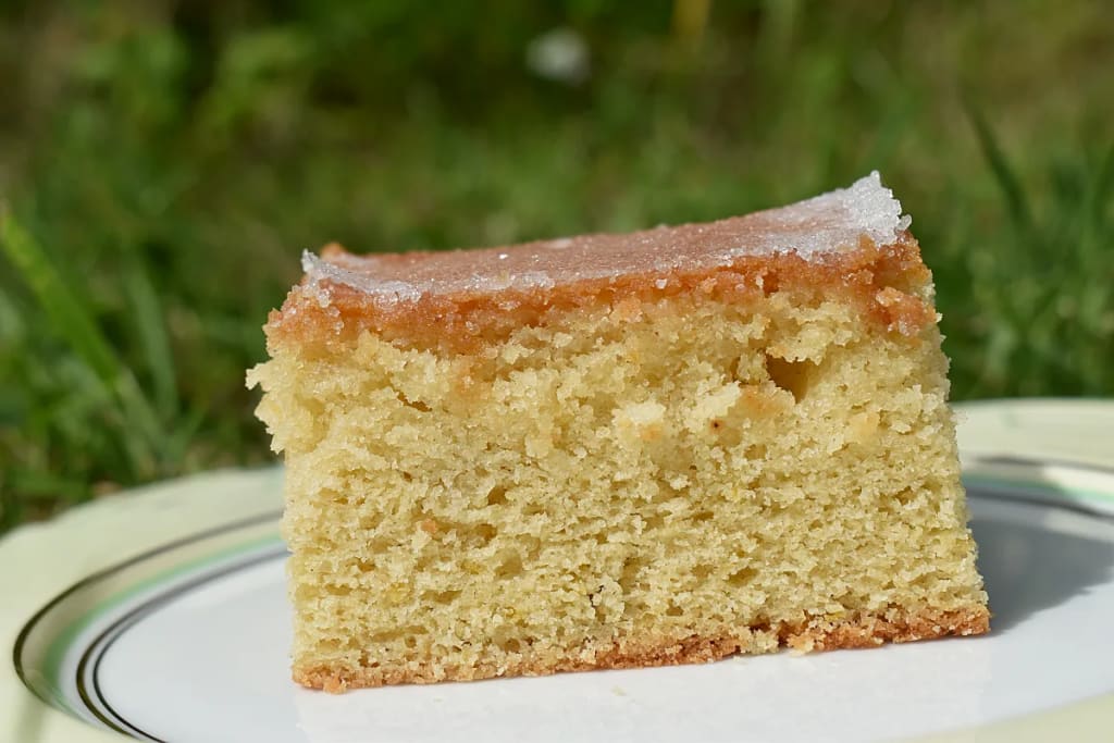 Lemon Drizzle Traybake slice on a plate in the garden in full sun.